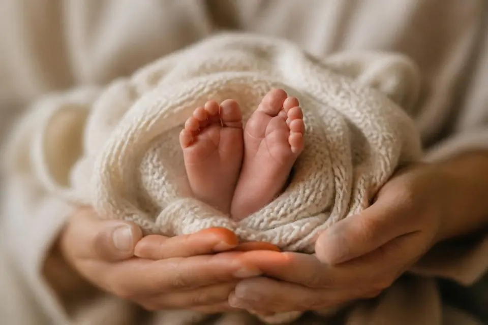 Newborn baby's feet in a cream knit blanket, held in a parent's hands