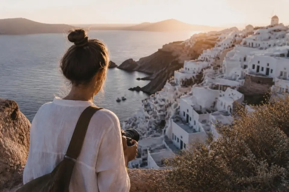 Traveler holding a camera overlooking a coastal village at golden hour