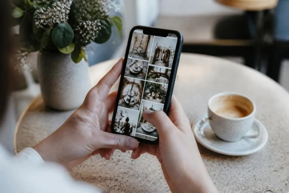 Hands holding a smartphone showing a grid of photos at a café table